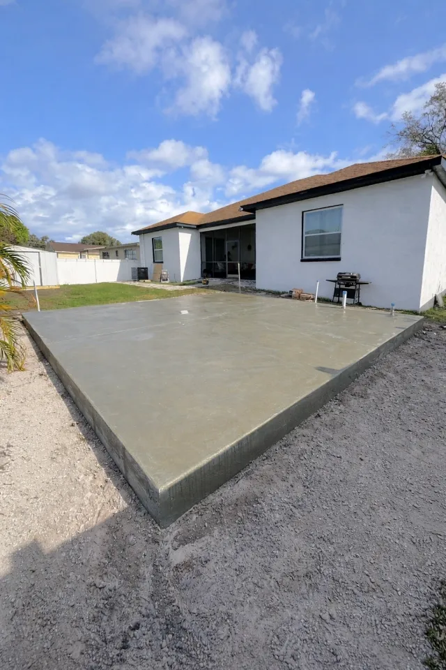 New concrete patio slab poured behind a white single-story home