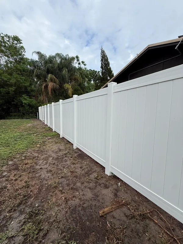 Long run of new white vinyl privacy fence along a backyard lined with palm trees